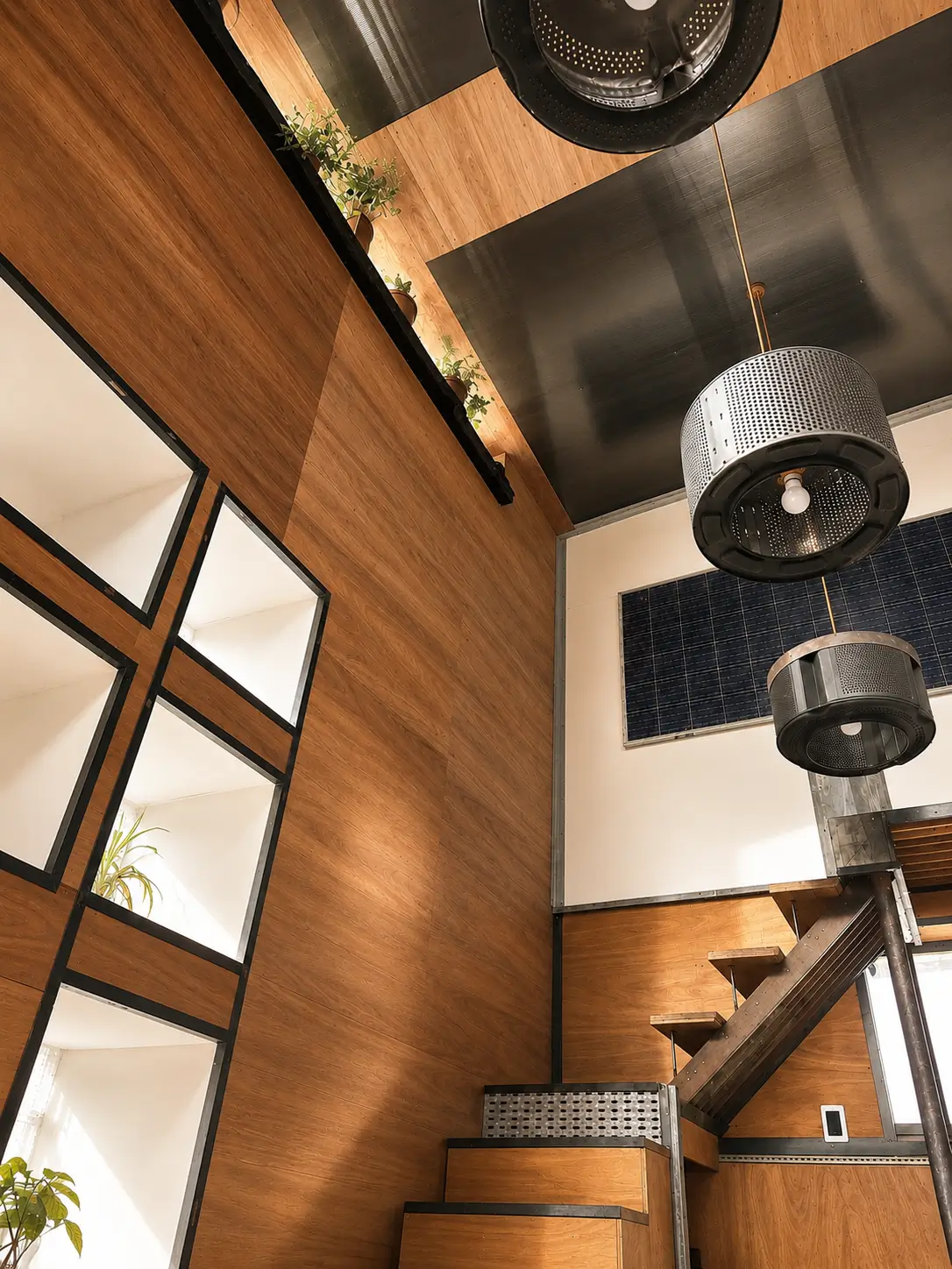Modern interior with wood-paneled walls, stairs, black light fixtures, and potted plants on a ledge.
