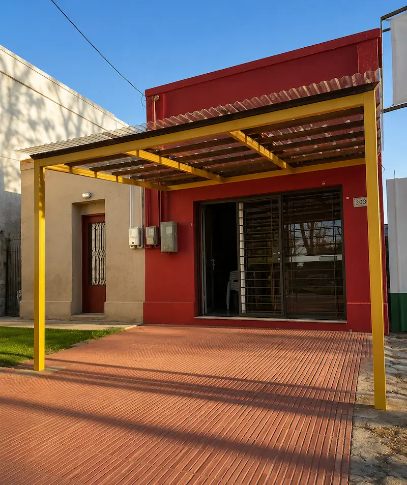 Yellow metal carport with corrugated roof in front of a red building with sliding glass door.